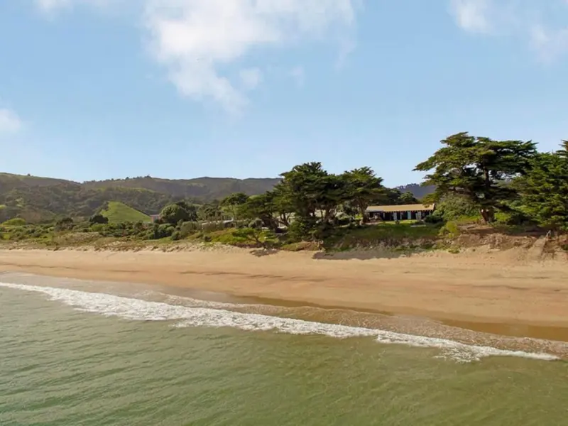 The house among old trees just behind the sand of Kuaotunu Beach, seen from the water