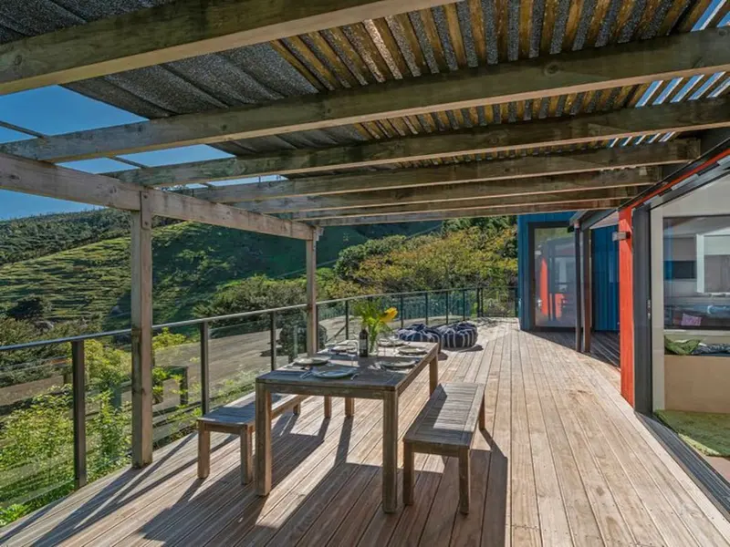 Covered deck with an outdoor dining table, looking across bush-clad hills