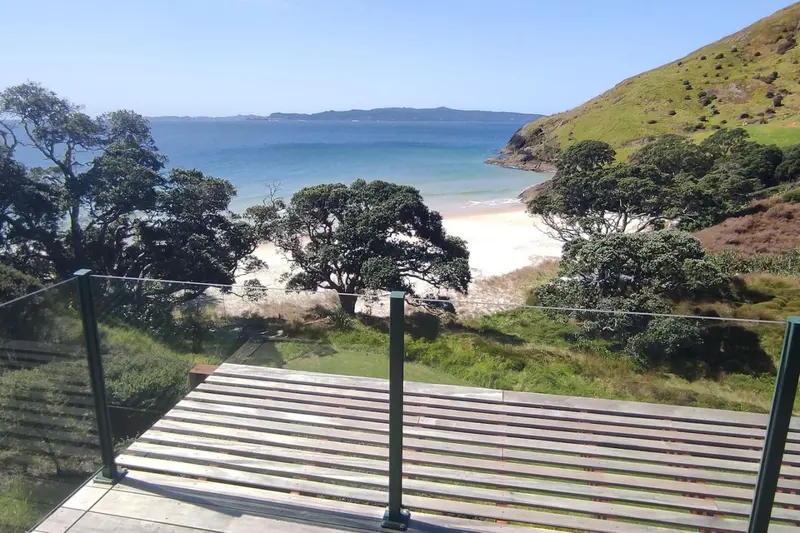 View from the deck over pōhutukawa to the white sand of Otama Beach and the sea