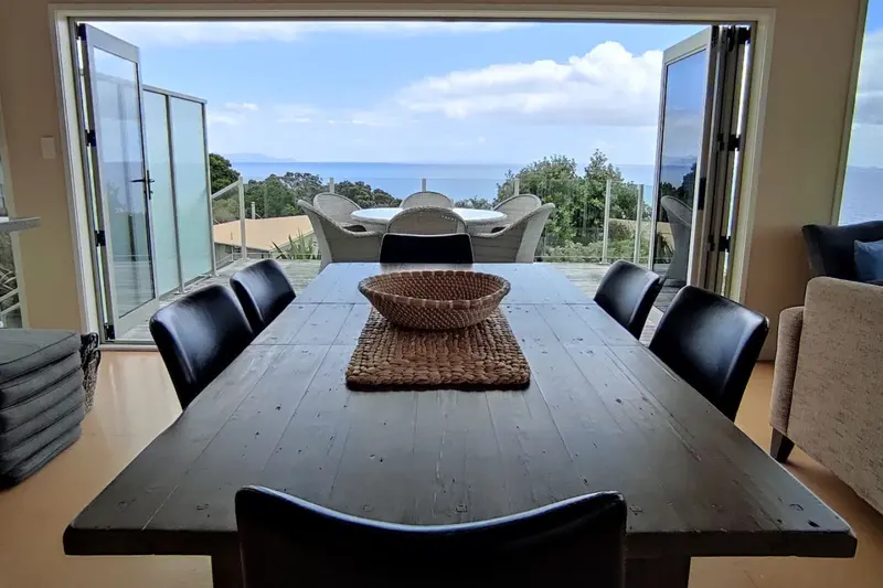 Dining table facing open bifold doors, the deck and the sea