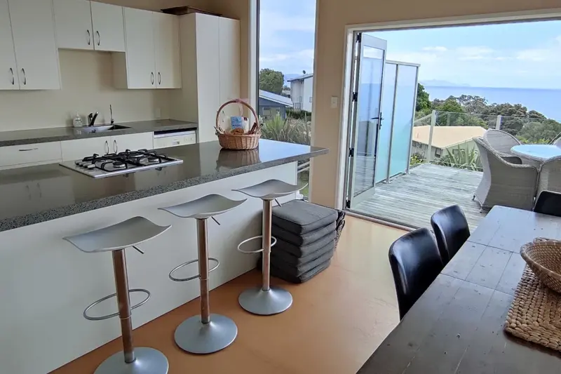 Kitchen bench with bar stools beside the open doors to the deck